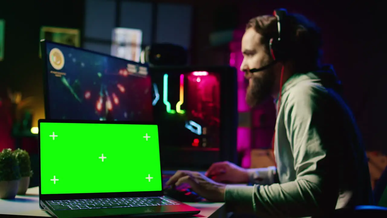 Chroma key laptop next to man playing high FPS singleplayer videogame with spaceship shooting lasers