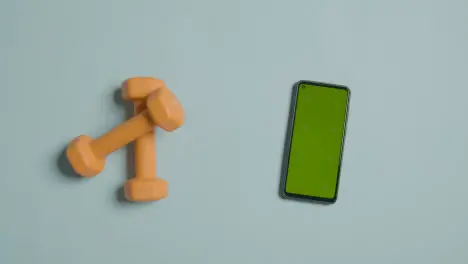 Overhead Fitness Studio Shot Of Male Hand Picking Up Exercise Dumbbell Weights Next To Green Screen Mobile Phone 1