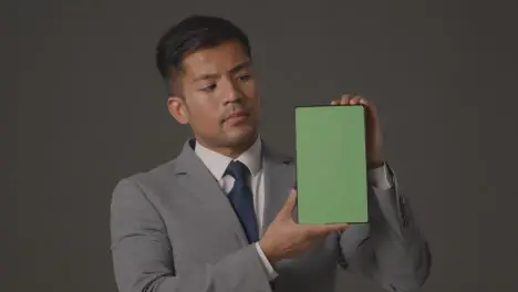 Studio Shot Of Serious Businessman In Suit Holding Green Screen Digital Tablet