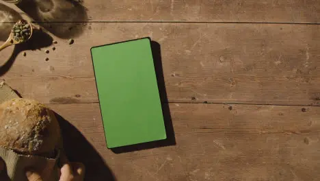 Overhead Shot Of Person Putting Down Loaf Of Bread From Wooden Table With Green Screen Digital Tablet