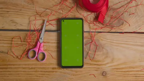 Overhead Shot Of Man Gift Wrapping Romantic Valentines Present In Box Next To Green Screen Mobile Phone