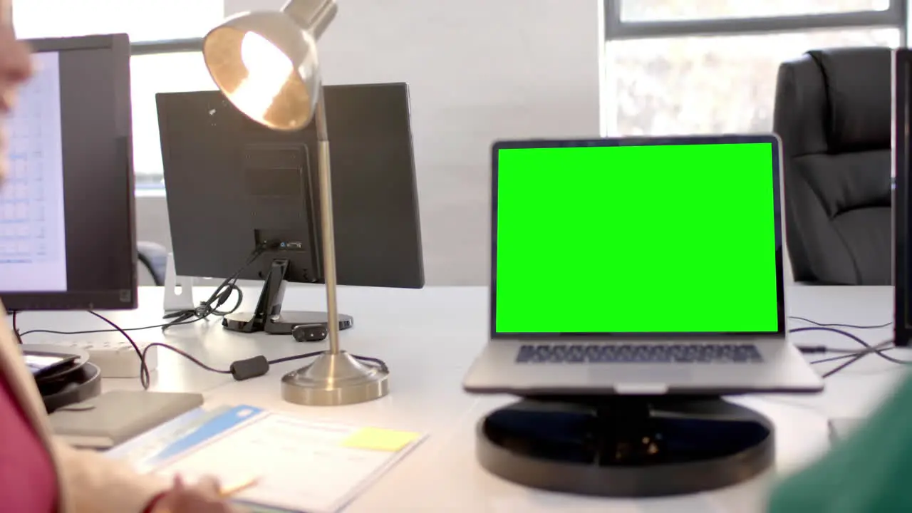 Opened laptop with green screen on desk in office