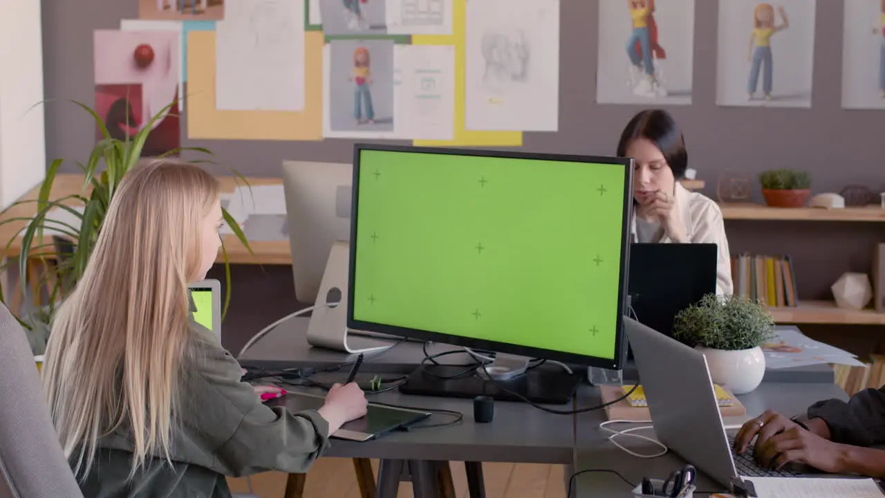 Female Graphic Designer Using Digital Drawing Tablet And Looking At Monitor With Green Screen In An Animation Studio