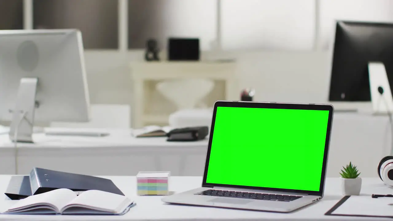 Laptop with green screen on desk in empty modern office space slow motion