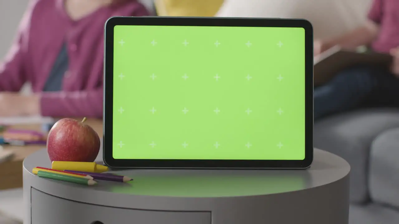 Close Up Of Green Screen Digital Tablet With Children Colouring And Reading In Background