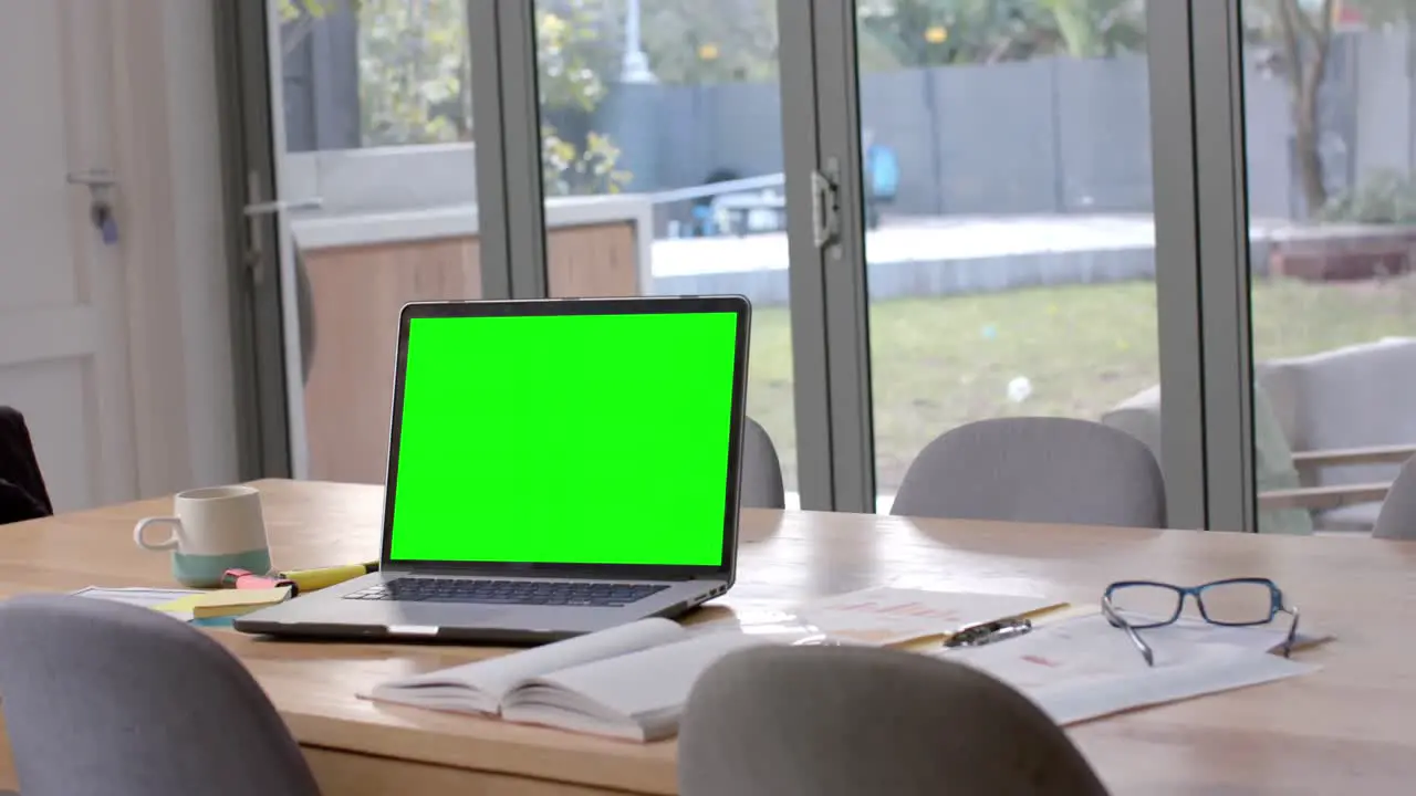 Laptop with green screen glasses and paperwork on dining table slow motion