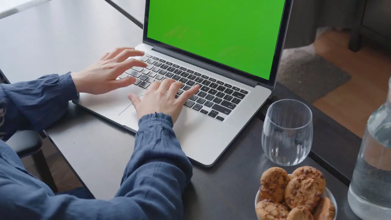 Over the shoulder shot of a woman typing on a computer laptop with a key-green screen