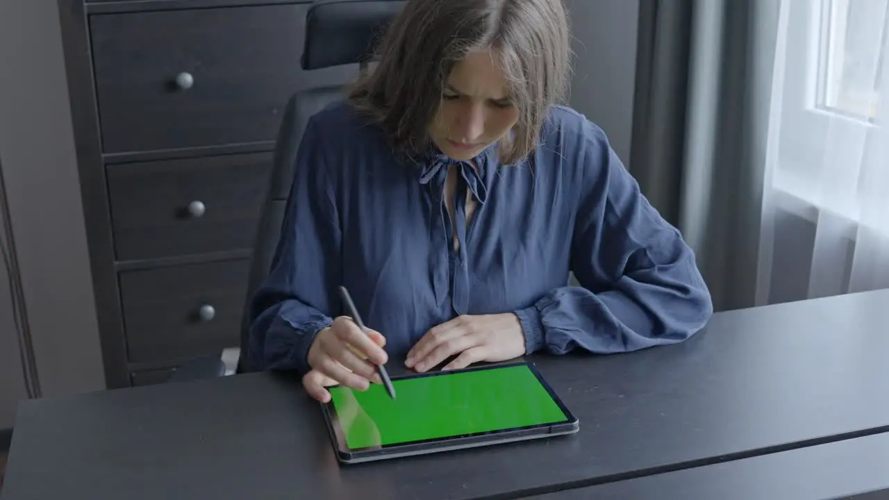 Woman is thinking while pointing at her green screen tablet in home office