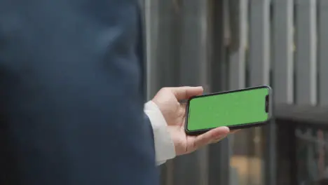 Businessman Outside City Of London Offices Holding Green Screen Mobile Phone Horizontally 2