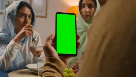 Man Looking At Green Screen Mobile Phone Sitting Around Muslim Family Table At Home Eating Iftar Meal Breaking Daily Fast During Ramadan 1