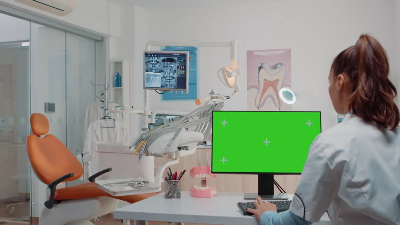 Woman working as dentist with green screen on monitor