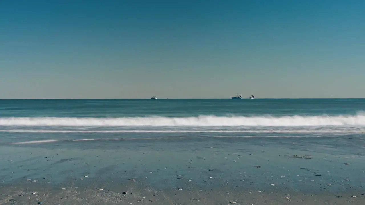 Timelapse of boats on ocean with waves pushing in and out in the foreground