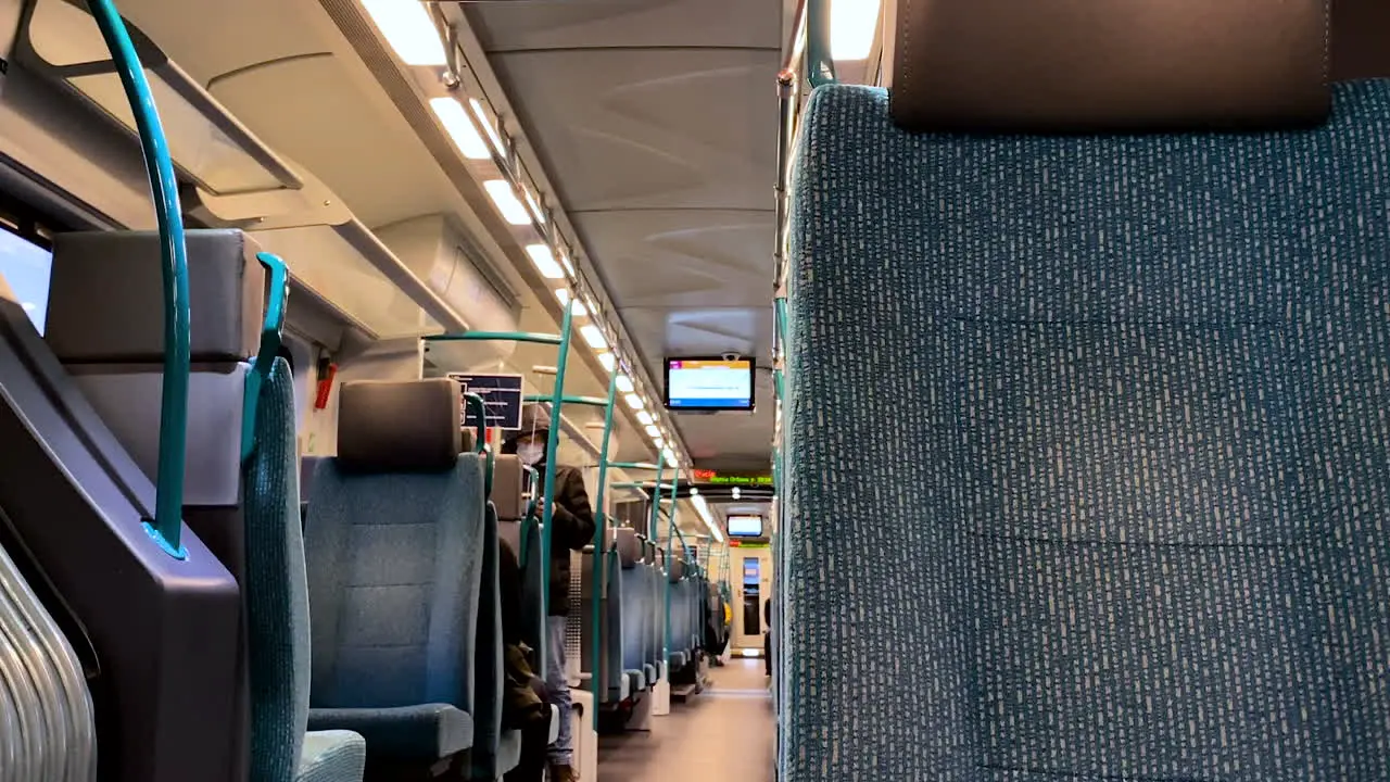 Slow pan right on railway train interior showing many empty seats and blurred people wearing masks on background