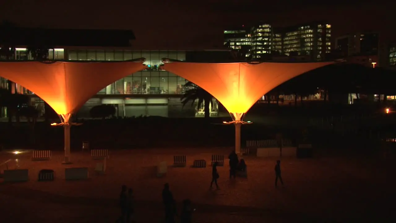 People walking in city center of Lisbon town late night time street lamps orange lighting black silhouettes of people walking near Lisbon Oceanarium entrance