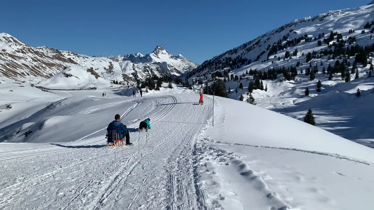 people having fun sledding on a field of snow with the alps in the background