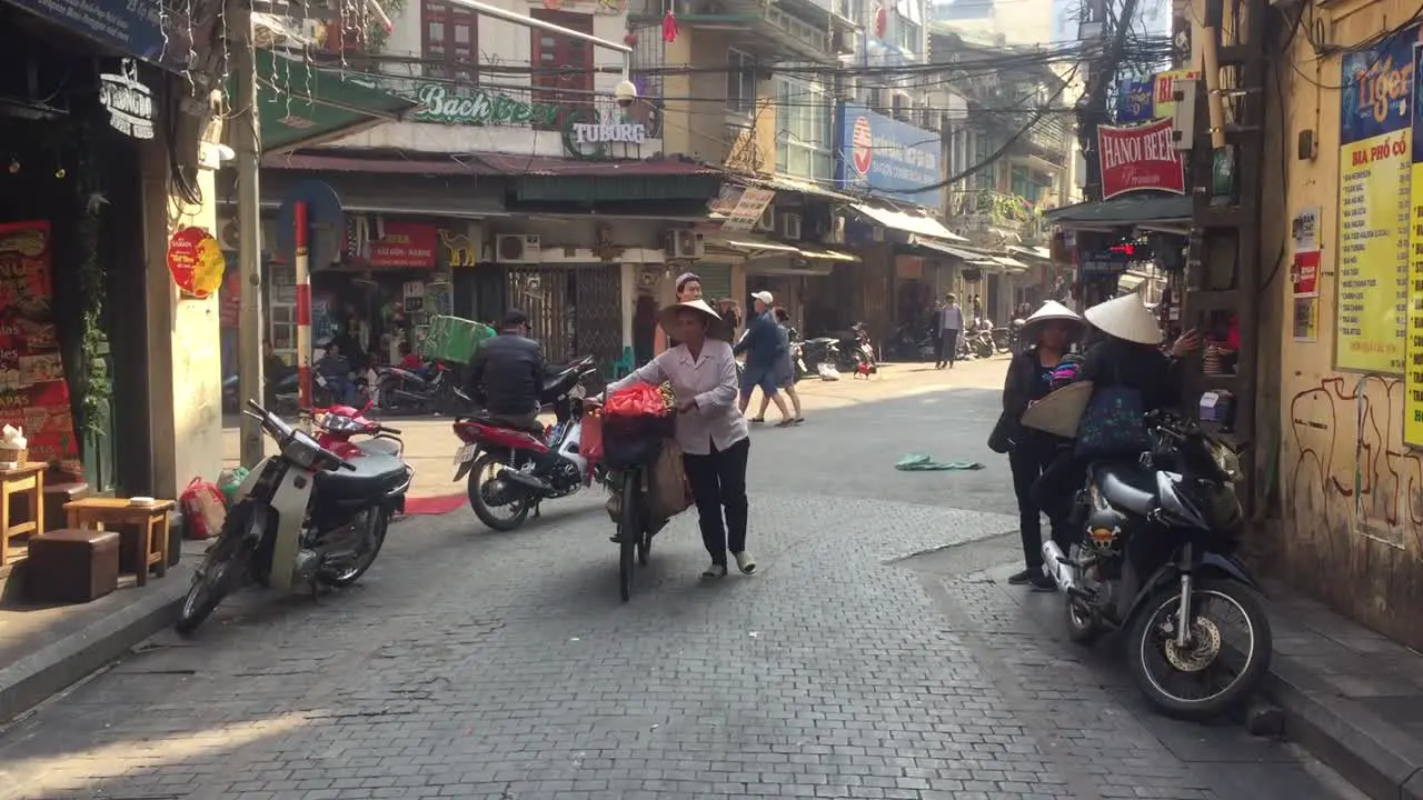 Woman walking bike and food down alley in Hanoi vietnam