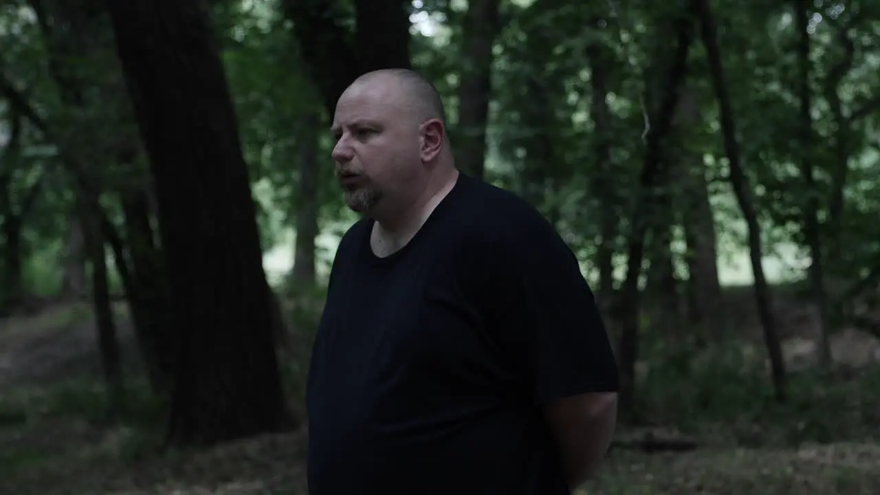 A man stands in forest contemplating and serious looking