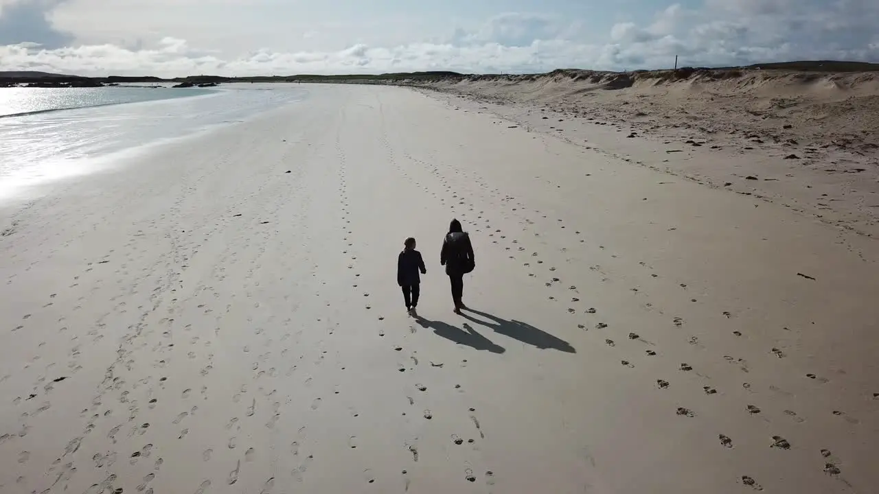 aerial push in two people walk on a large sandy beach in Connemara Ireland