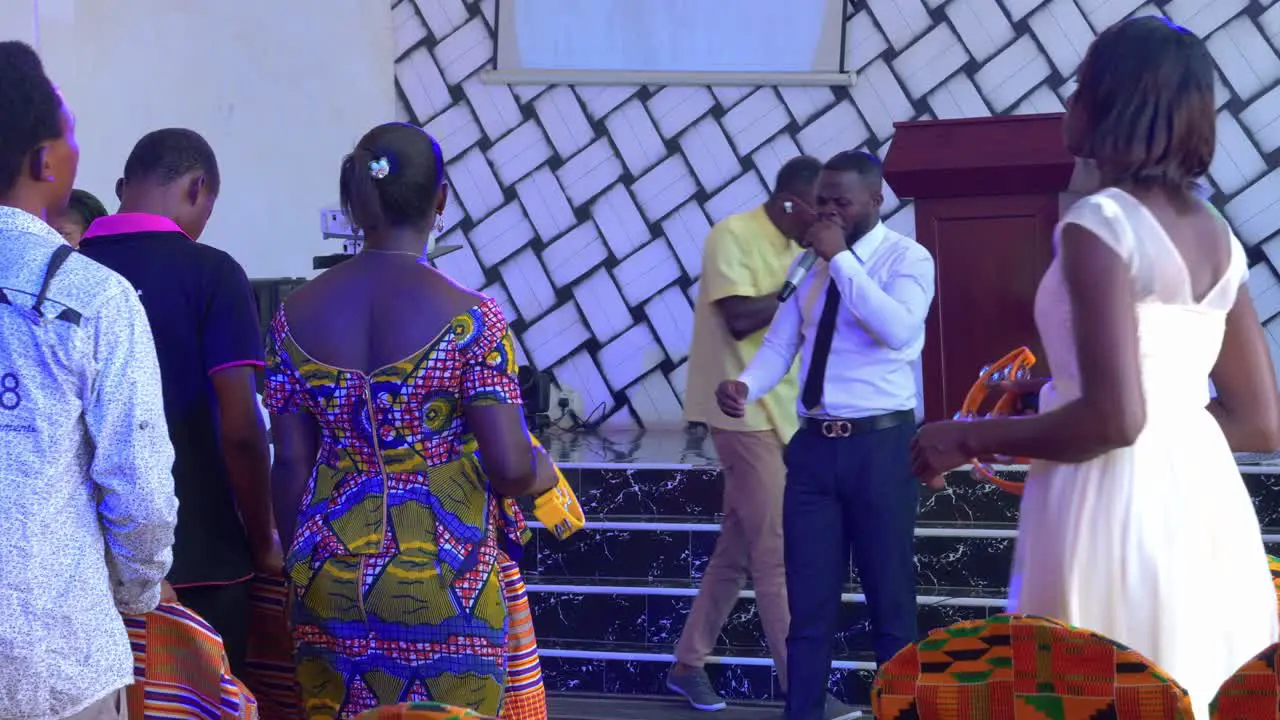 Two African young men singing effusively with a microphone while women dance