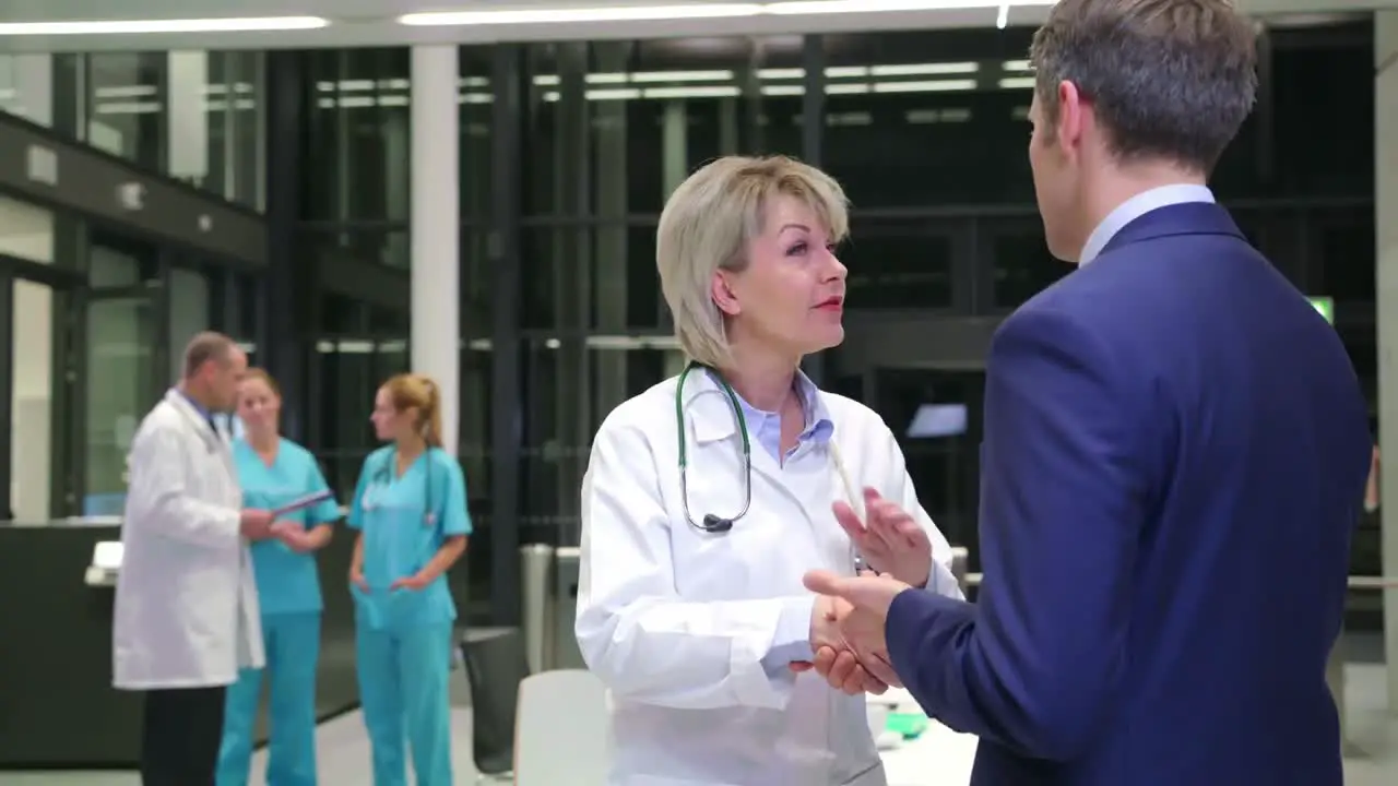 Female doctor shaking hands with businessman in corridor