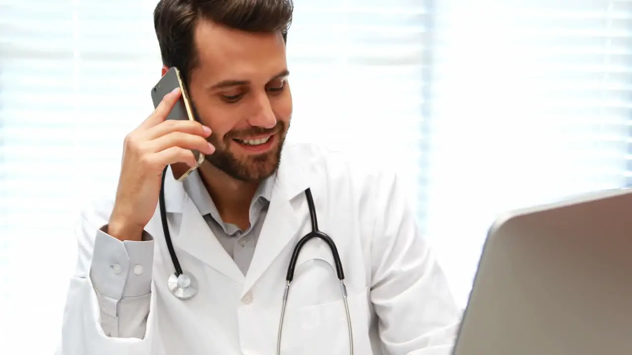 Male doctor talking on mobile phone while working on computer