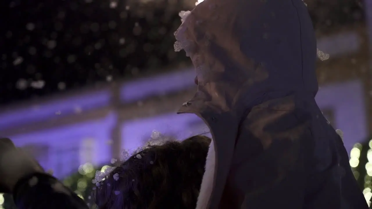 Slow motion handheld shot of people standing at a christmas party with a winter jacket while it is snowing