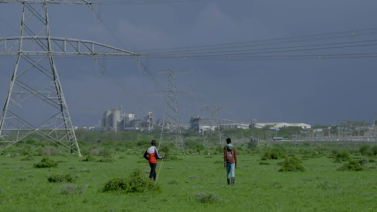 Two black men walk through a green meadow on the edge of a city