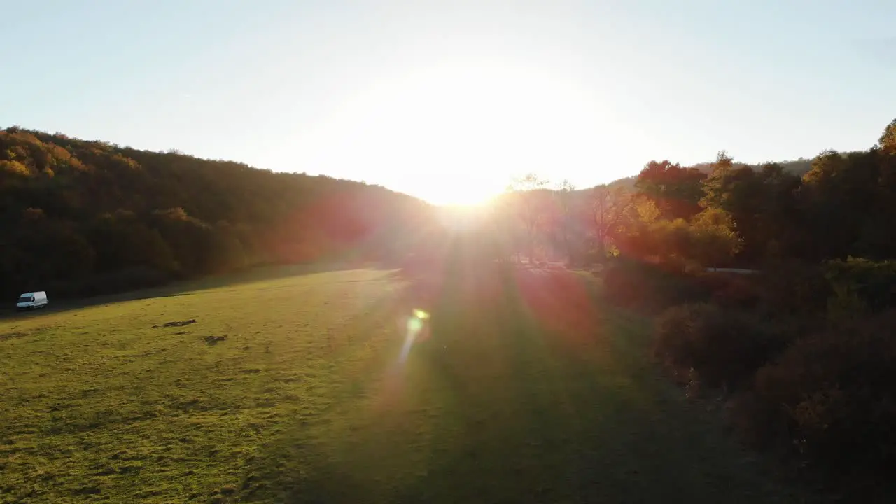 Aerial epic drone shot of sun rays in grass field surrounded by forest at sunset-5