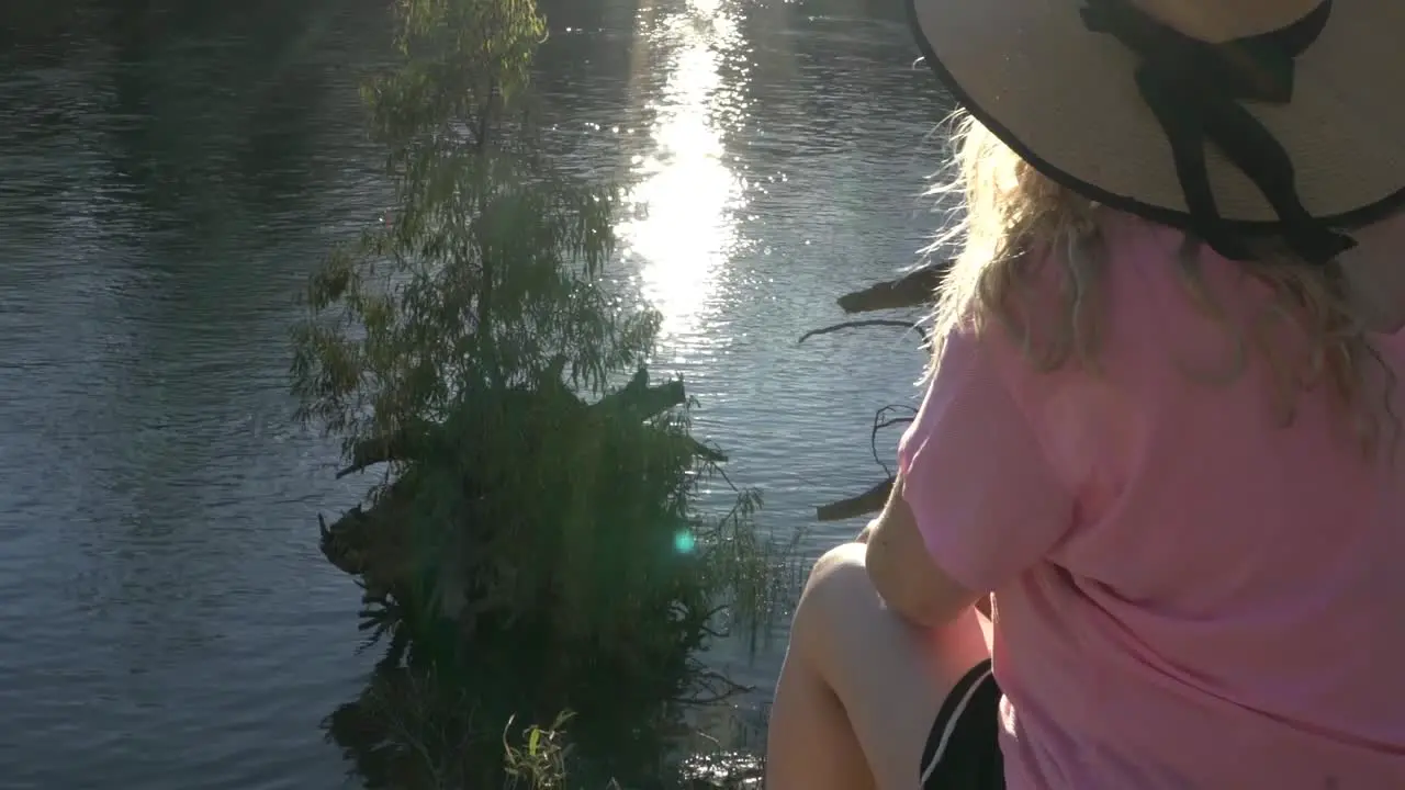 Outdoor nature blonde woman sitting in river edge wearing pink top camping