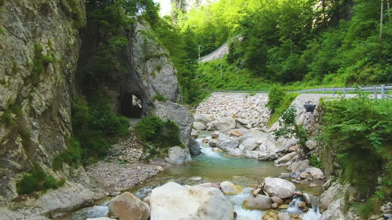 Clear shallow river with stones surrounded by rocks greenery and traffic road