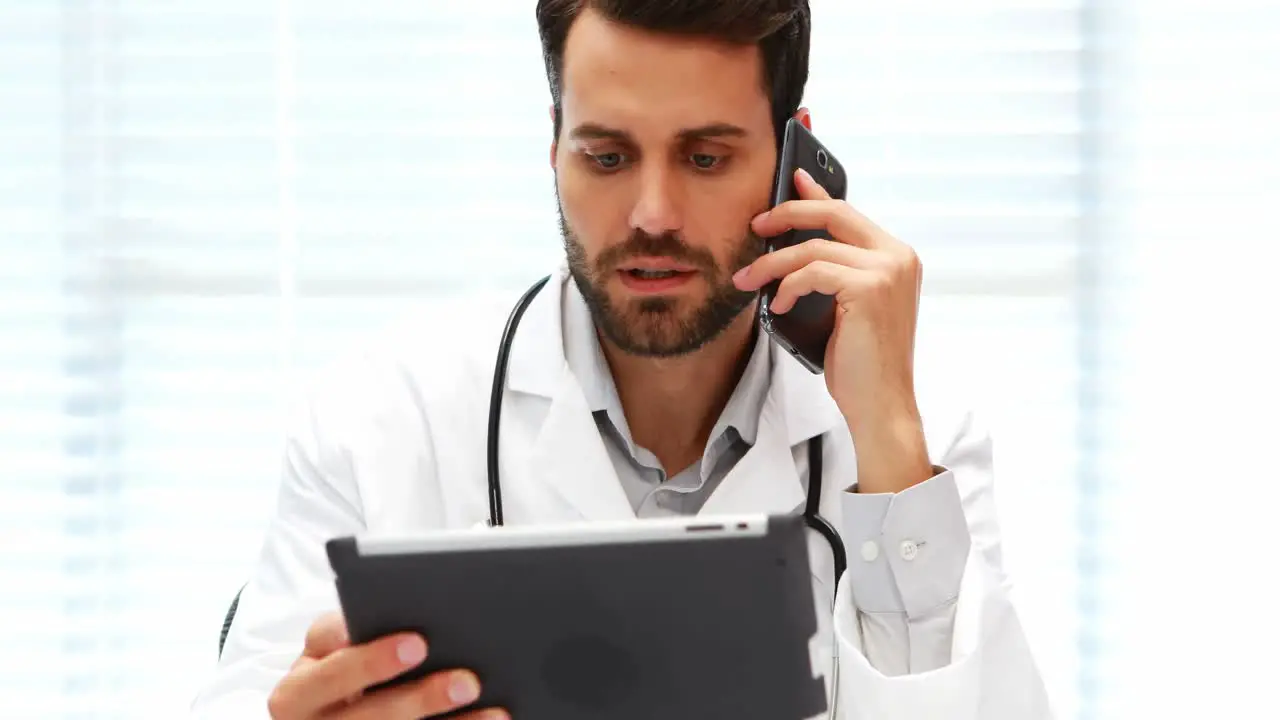 Male doctor talking on mobile phone while using digital tablet