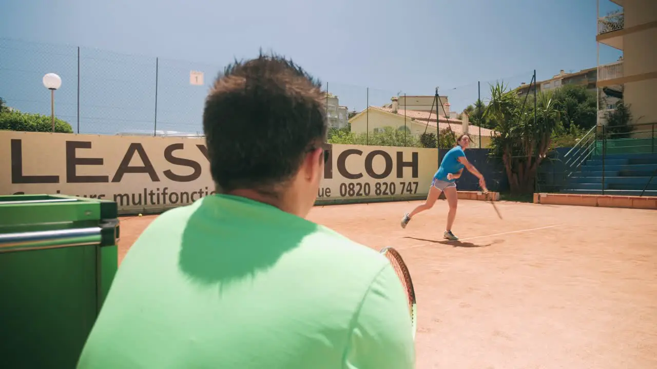 Over the shoulder of tennis teacher and student learning to serve