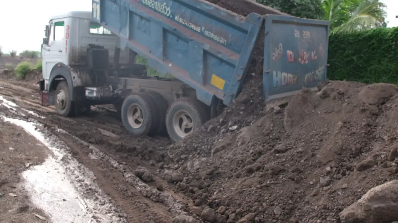 A slow motion scene in which a large loader truck unloads soil from its truck preparing to avoid a road block due to heavy rain