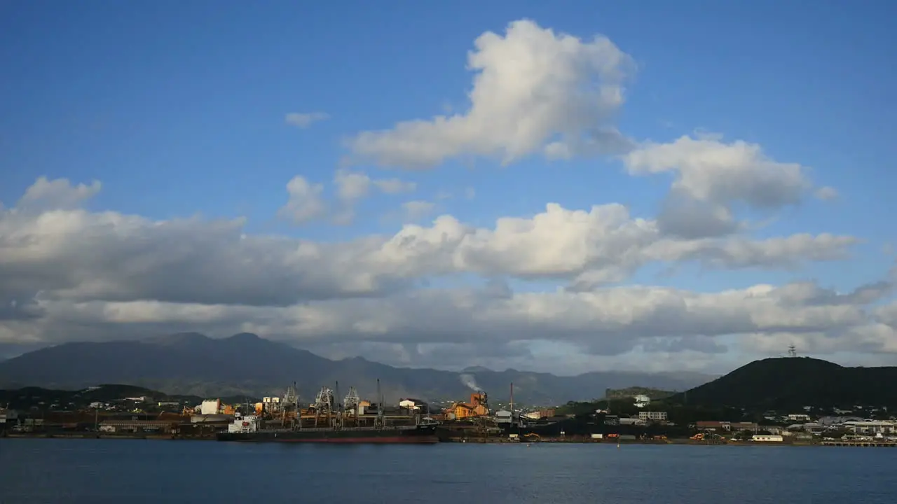 New Caledonia Cumulus Clouds Rise In Blue Sky Above Waterfront Industrial Plants