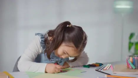 Shot Of Young Girl At Table At Home Drawing And Colouring In Picture 1