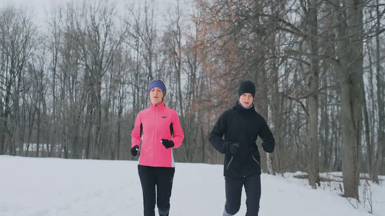 Young family couple man and woman on a morning jog in the winter forest A woman in a loose jacket a man in a black jacket is running through a winter park Healthy lifestyle happy family