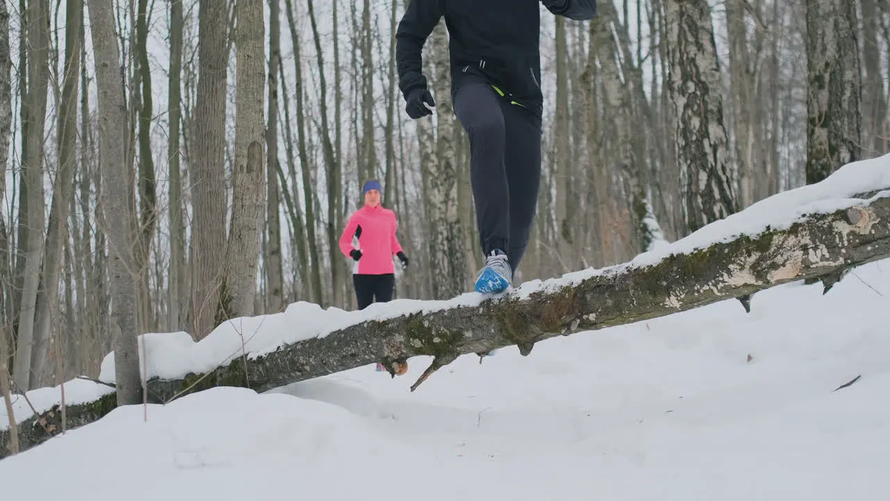 A man and a woman run in the park in winter and jump over a fallen tree Step over the obstacle