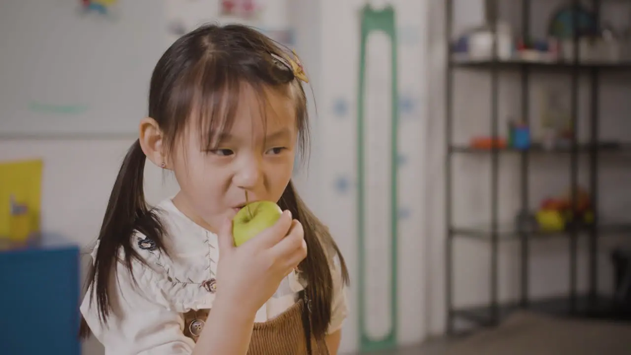 Little Girl Eating An Apple In Classroom In A Montessori School