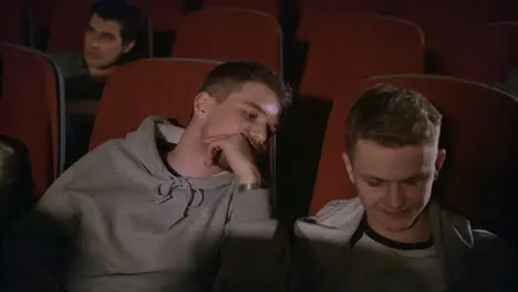 Two guys looking smartphone in cinema Friends having fun with phone at theatre