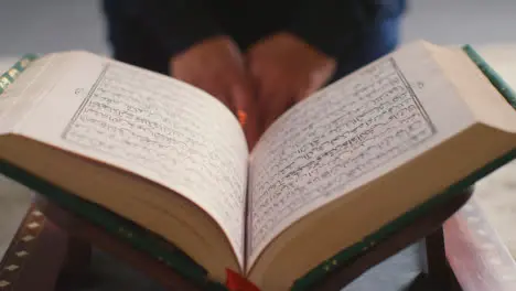 Close Up Of Open Copy Of The Quran On Stand At Home With Woman Sitting Behind 1