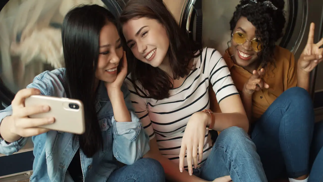 Three Pretty Mixed Races Friendly Girls At Washing Machines In Washhouse Smiling To Smartphone Camera Taking Selfire Photo