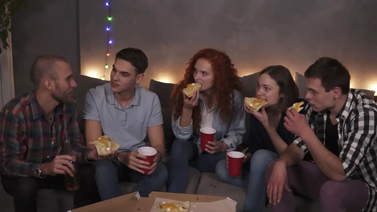 Young People Cheerful Men And Women Are Eating Cheesy Pizza Chatting Relaxing During Indoor Party In Apartment In A Loft Room