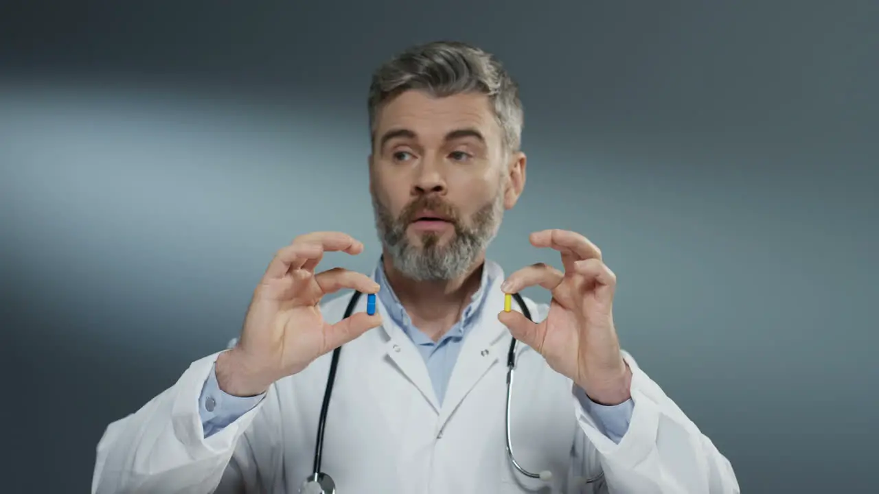 Male Physician Holding Two Pills In Hands One Yellow And One Blue While Comparing Them And Studying Carefully