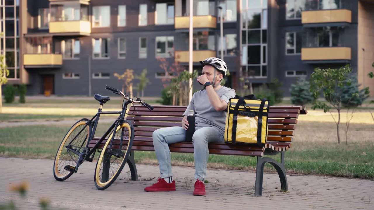 Food Delivery Guy Seated On A Bench Having A Cup Of Tea During His Break