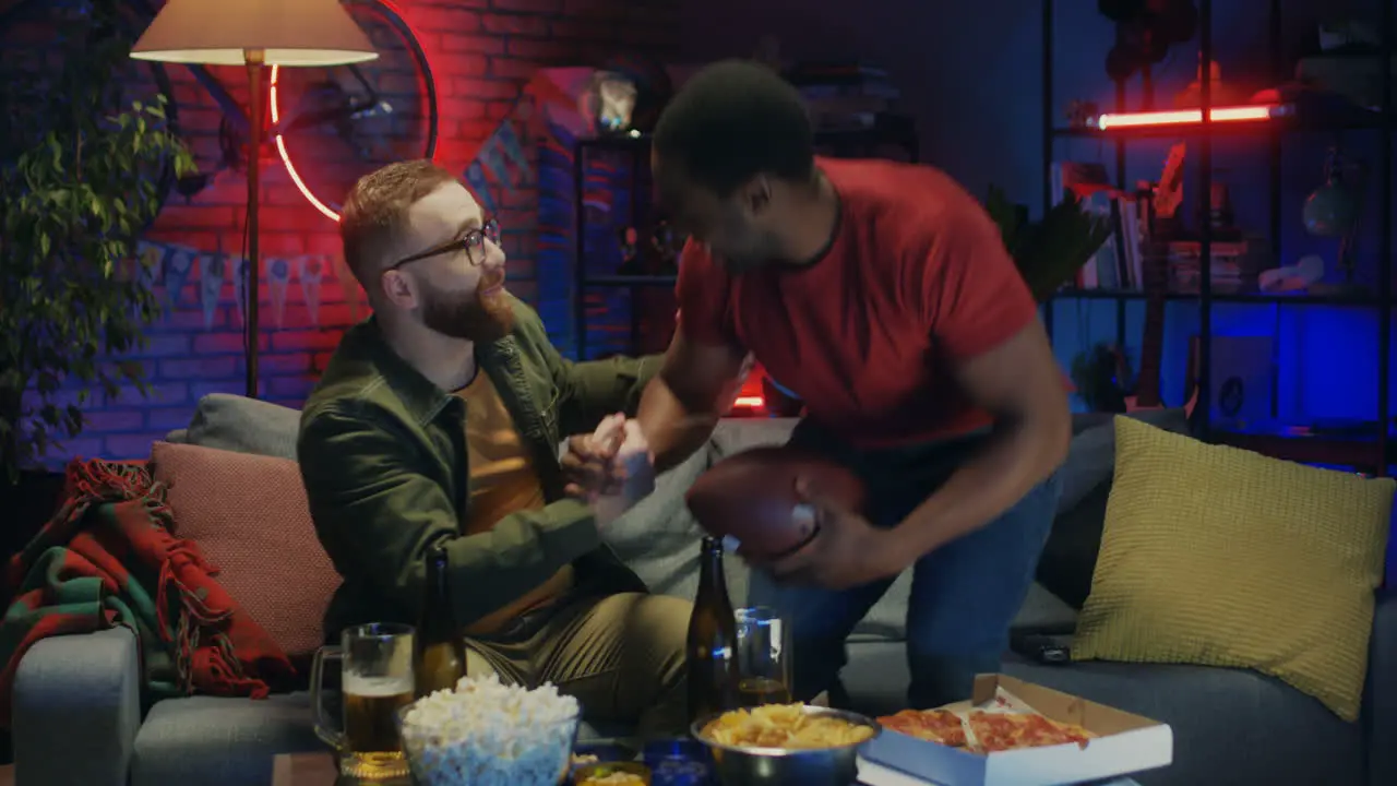 Young Guy Coming Into The Dark Room To His Male Friend Sport Fans Watching Sport Match On Tv Together And Cheering