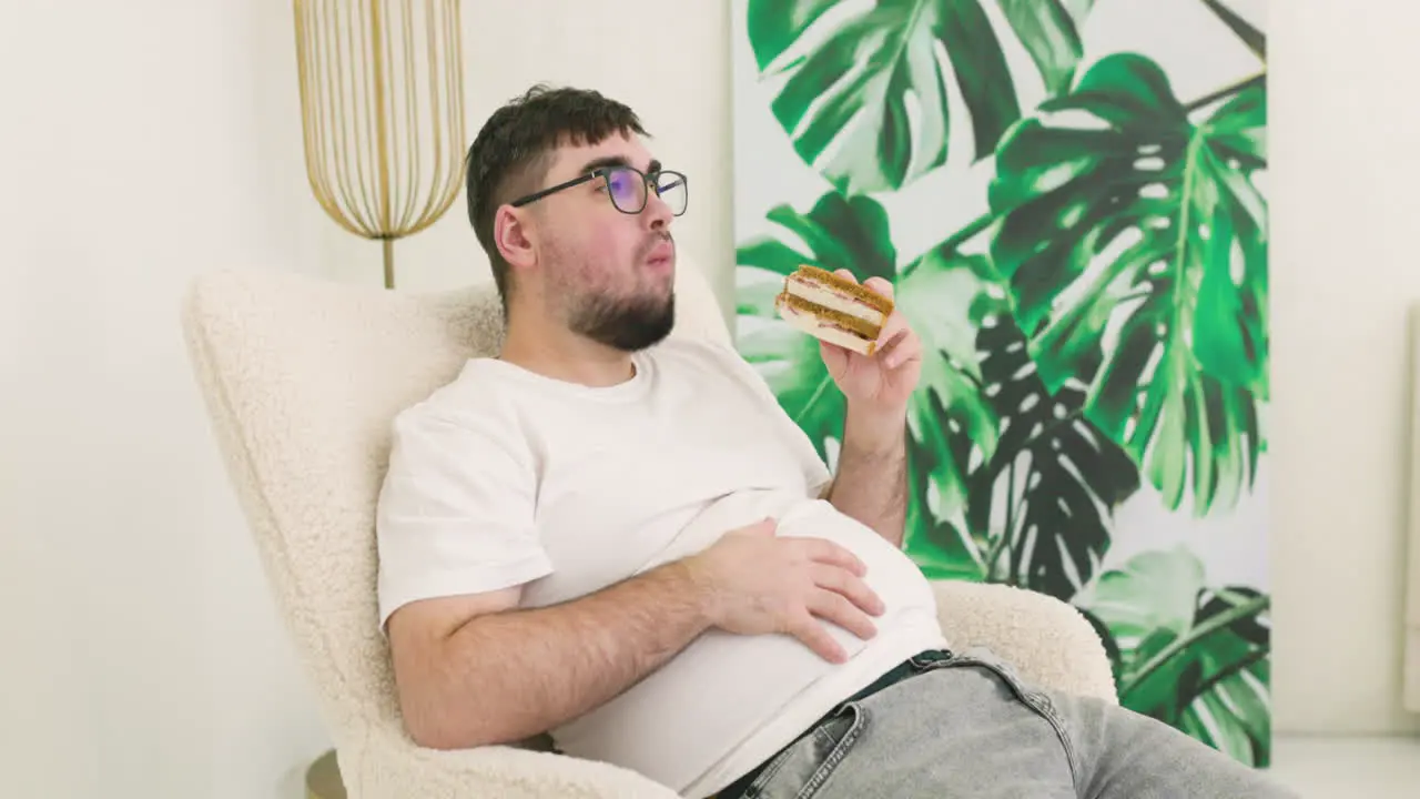 Boy Touching His Belly Fat And Eating A Sandwich Sitting On Sofa