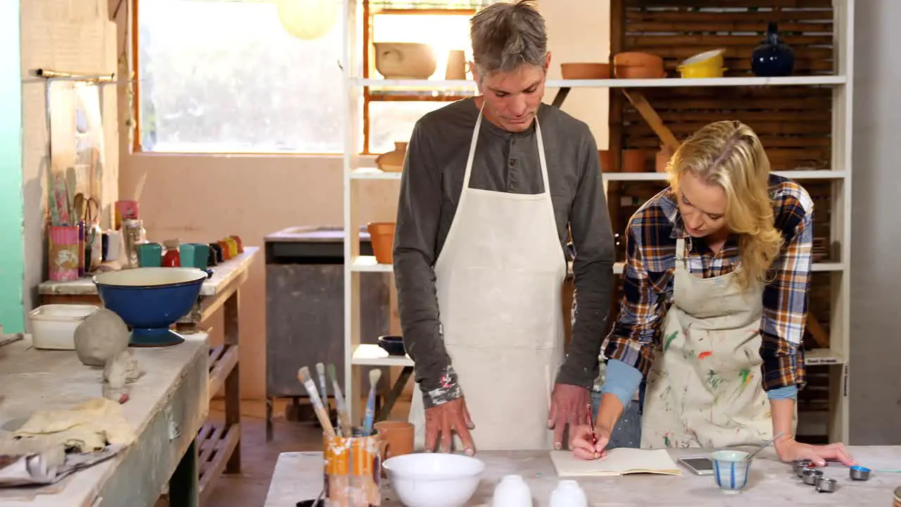 Male and female potters writing on a book