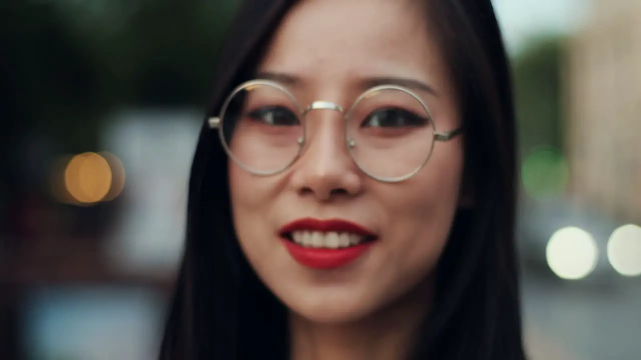 Portrait Of The Young Attractive Woman In Glasses Smiling To The Camera Cheerfully Outdoors At The Street First Blurred And Then In Focus