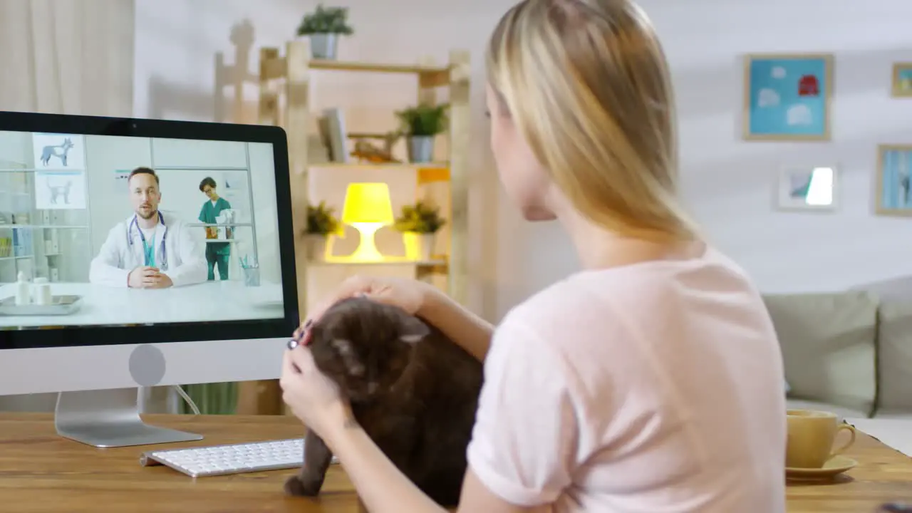 Blonde Woman With Her Black Cat Talking To A Vet In An Online Consultation