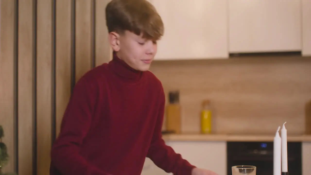 Camera Focuses On A Boy Placing A Milk Glass And A Plate Full Of Cookies On An Empty Table With Two Candles Then He Leaves The Room